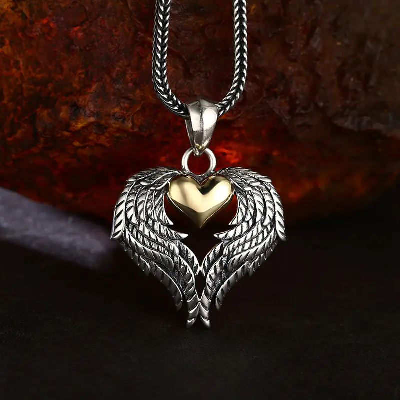 Front lifestyle view 925 silver angel wing pendant with two‑tone gold heart, intricate feather carving against textured rust rock background