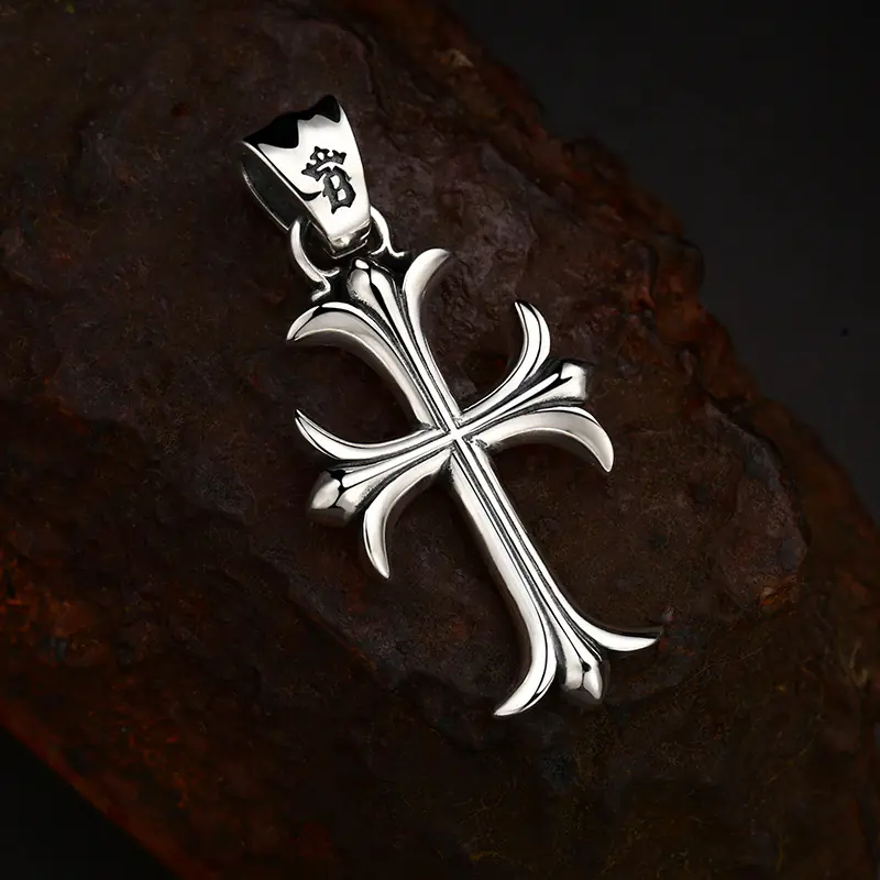 Tilted flat‑lay view 925 sterling silver gothic fleur‑de‑lis cross pendant, shows sculpted contours and engraved logo on decorative bail