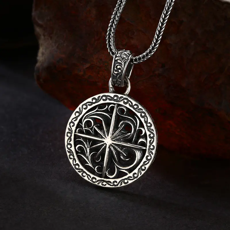 Slight side‑angled shot of vintage oxidized 925 silver compass medallion pendant, showing rim engraving and hollow star‑scroll details on rust rock background